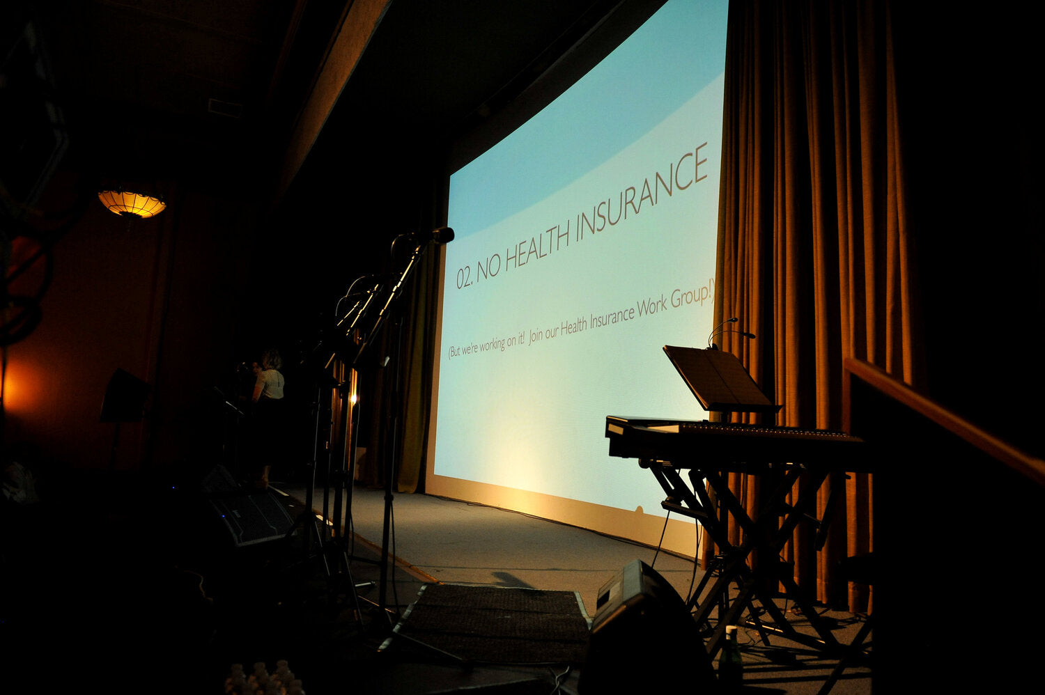 A stage setup that has a presentation on the screen that says "02. No Health Insurance"